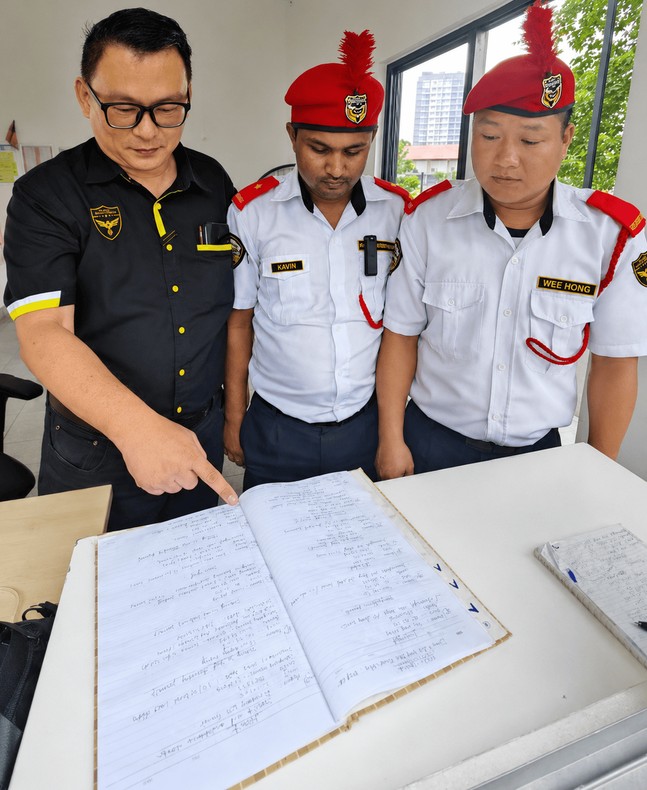 Manager reviewing a guardhouse occurrence logbook with two officers